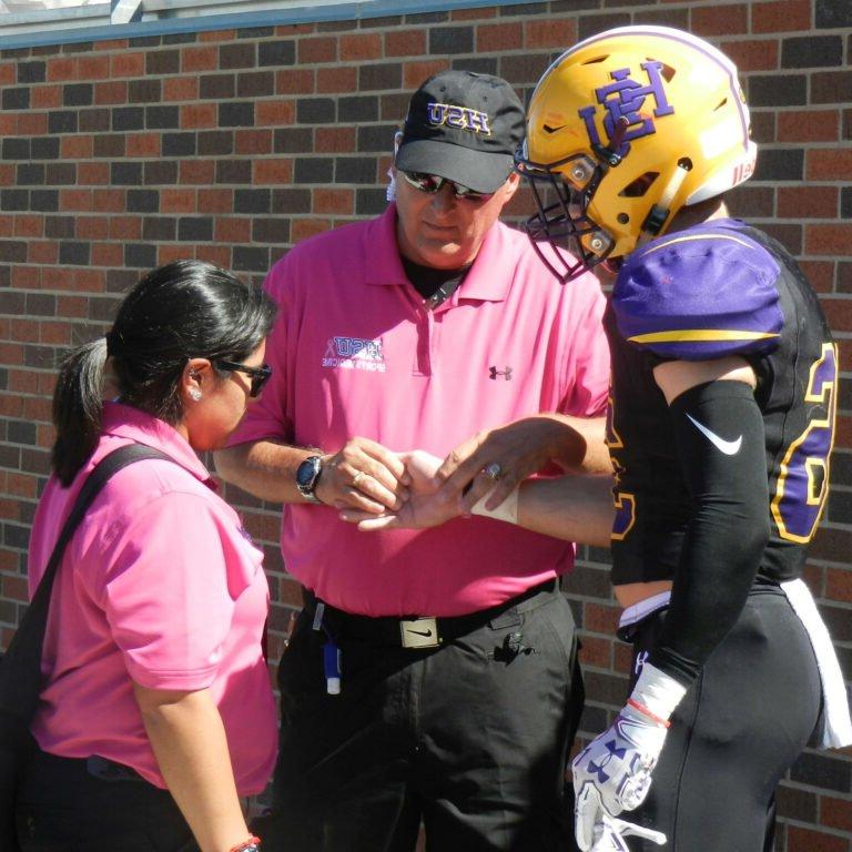 An athletic training professor wraps a football player's wrist as a student trainer observes.